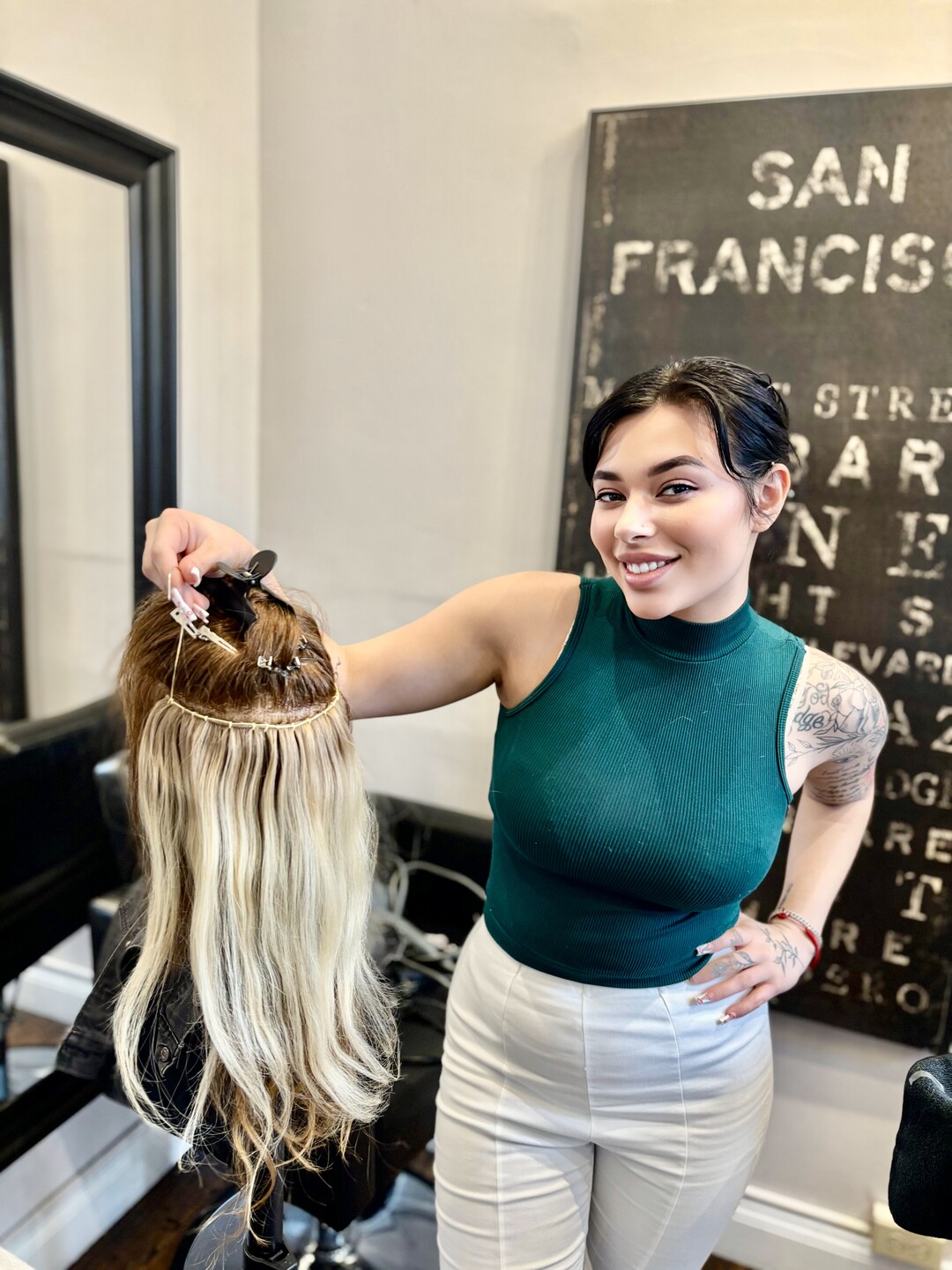 A blonde balayage weft held against a dark head, under the San Francisco sign