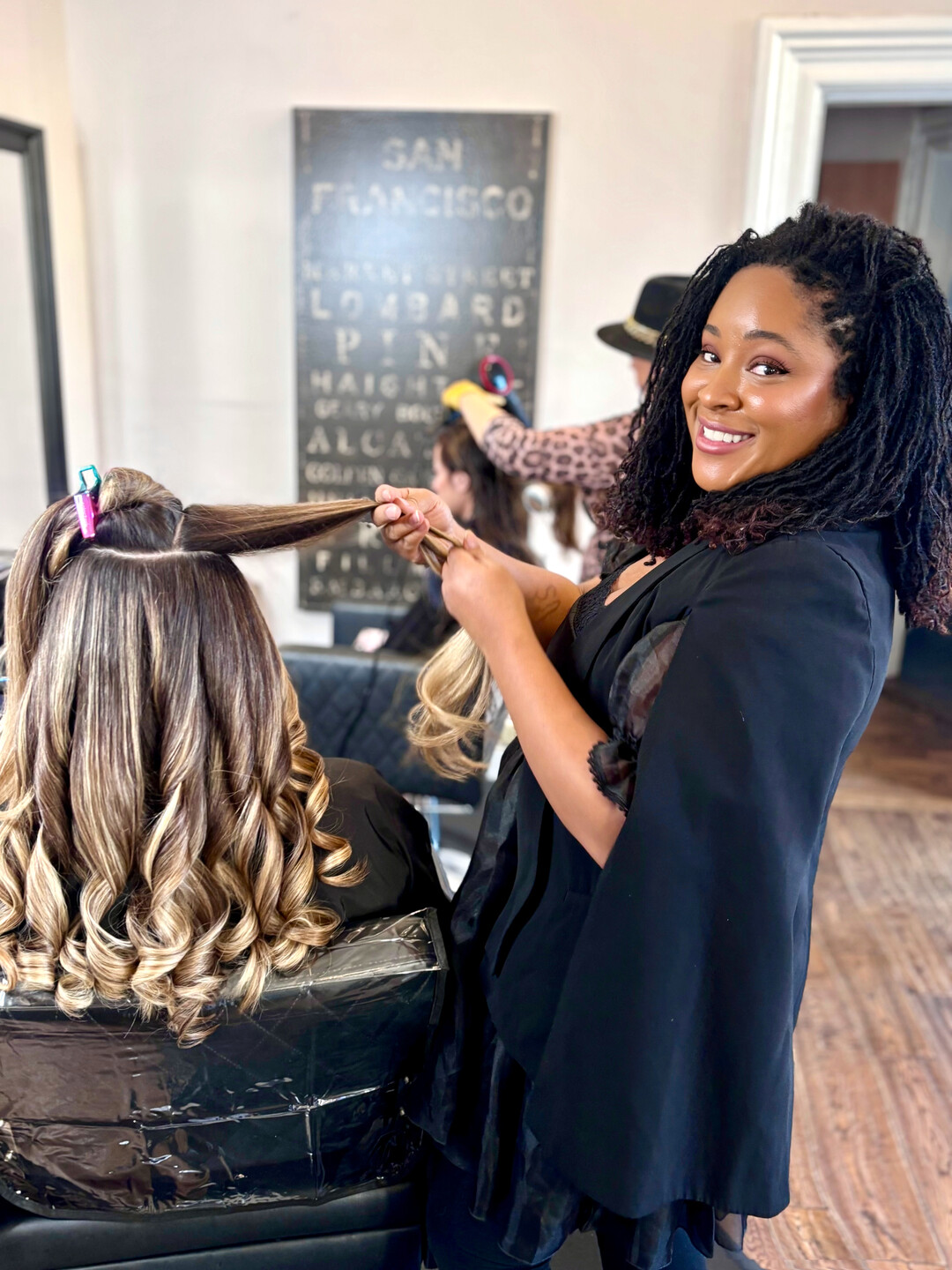Long curled brunette-into-blonde extensions being finished on a seated client