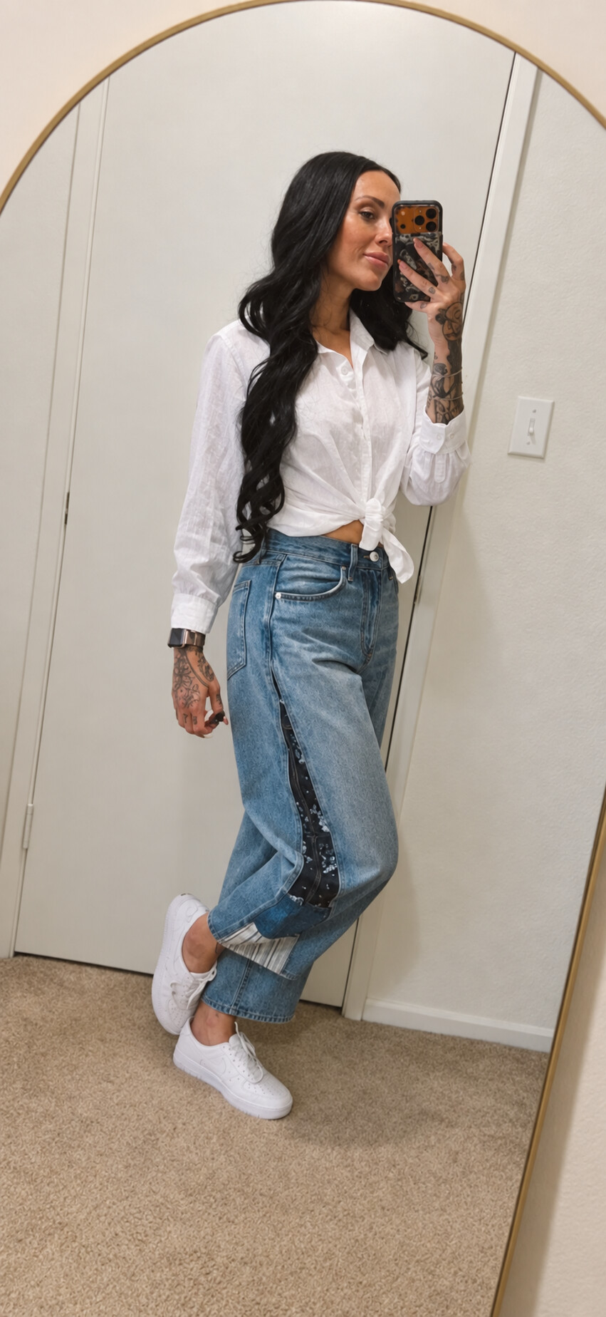 Frankie taking a mirror selfie, her long dark waves falling over a knotted white shirt and blue jeans