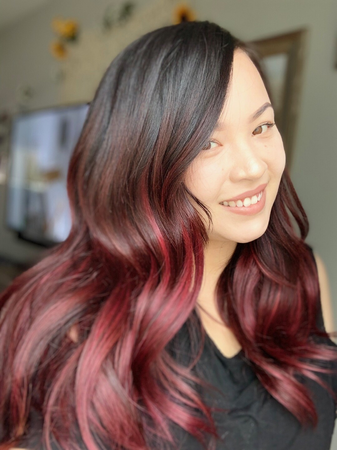 A smiling client with wavy hair past the shoulders, black at the root and red at the ends