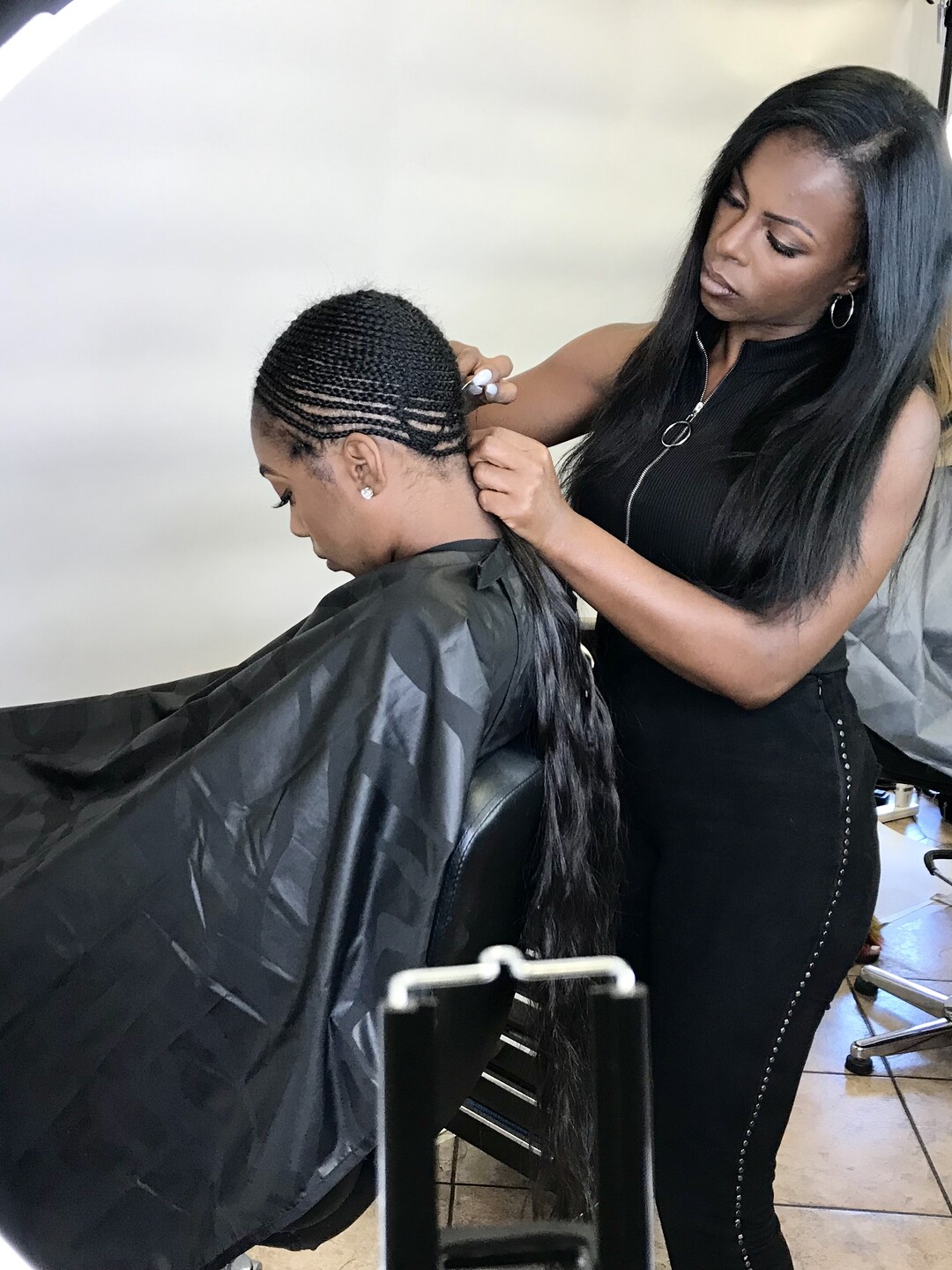A stylist sectioning a client’s dark hair and sewing in a weft at the crown