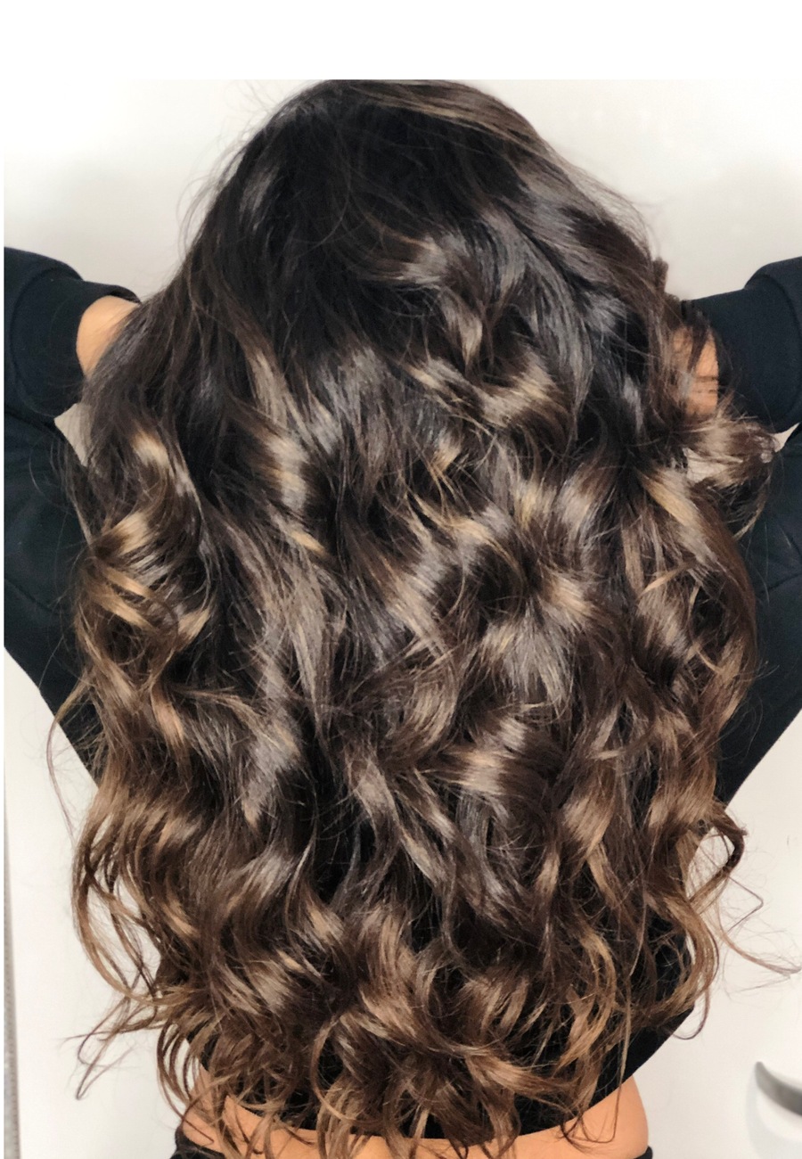 Dimensional brunette hair curled loosely, with caramel ribbons through the mid-lengths