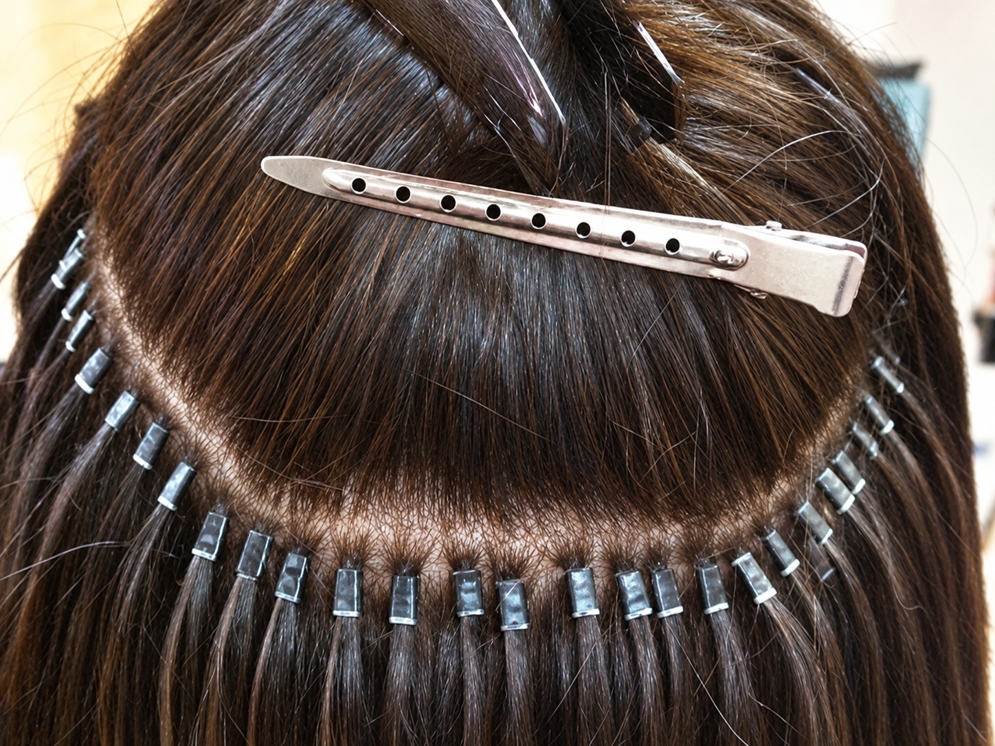 Small matte beads along a parting in long dark hair, each holding a strand, under a silver clip