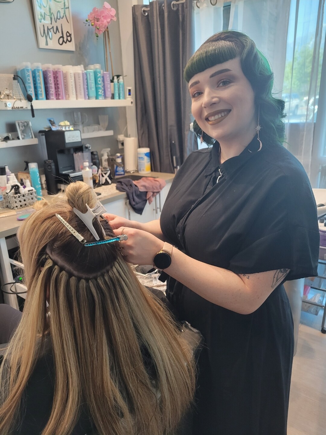 Sandie’s stylist behind a client, closing a row of beaded wefts at the salon