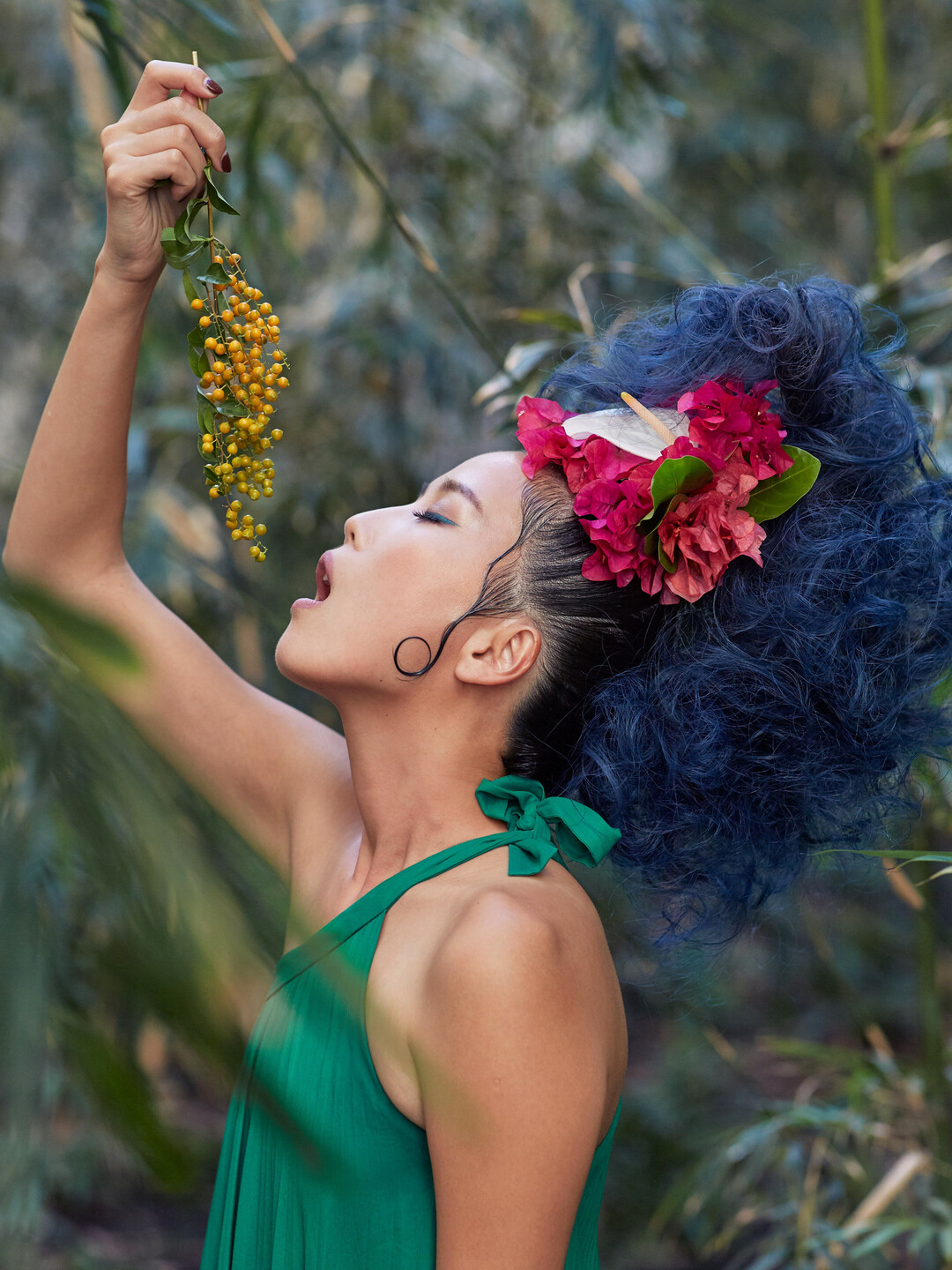 Sculptural blue hair decorated with pink flowers, photographed in profile outdoors